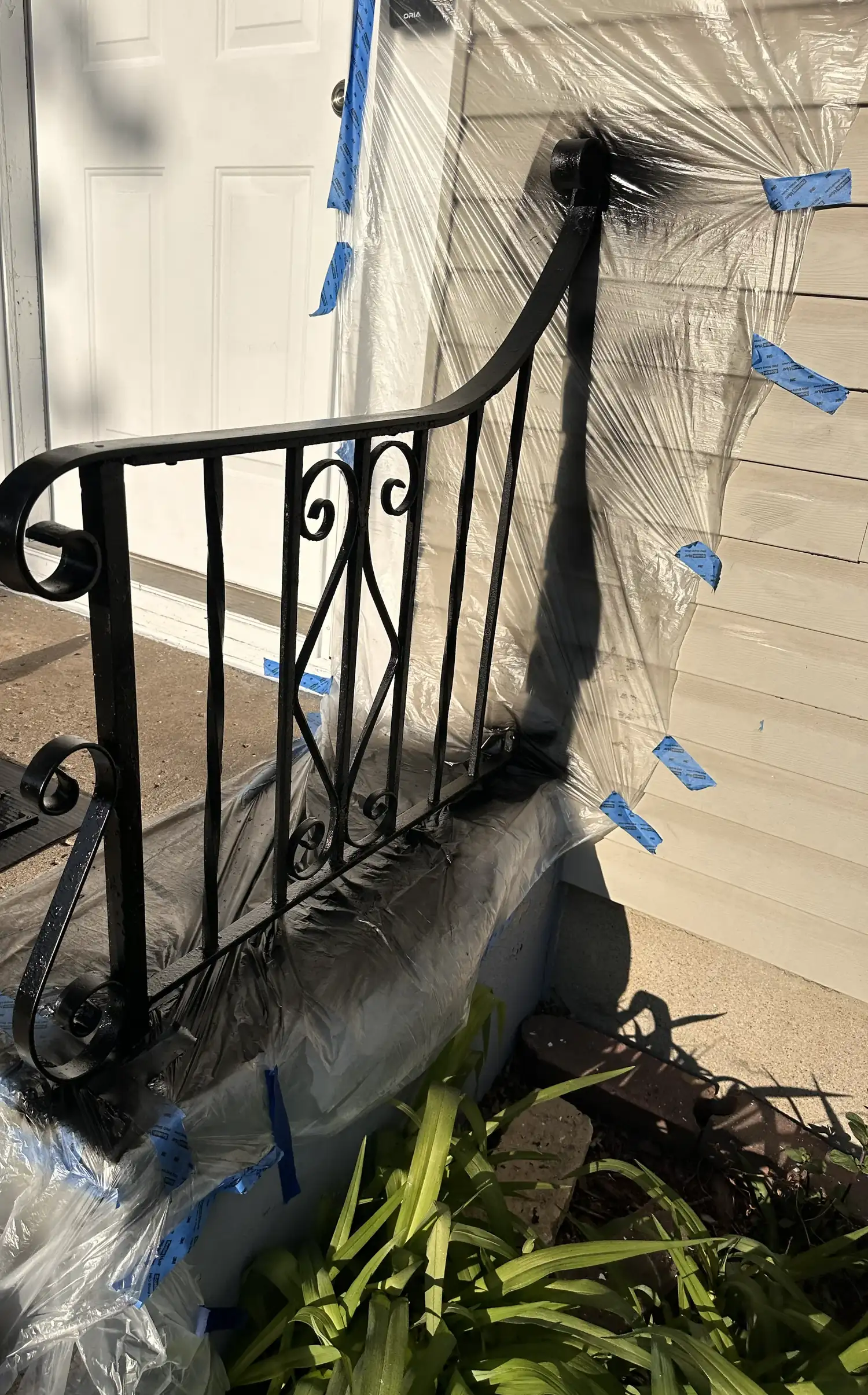 The same wrought iron railing after being stripped, primed and repainted gloss black, with the siding and plantings masked off