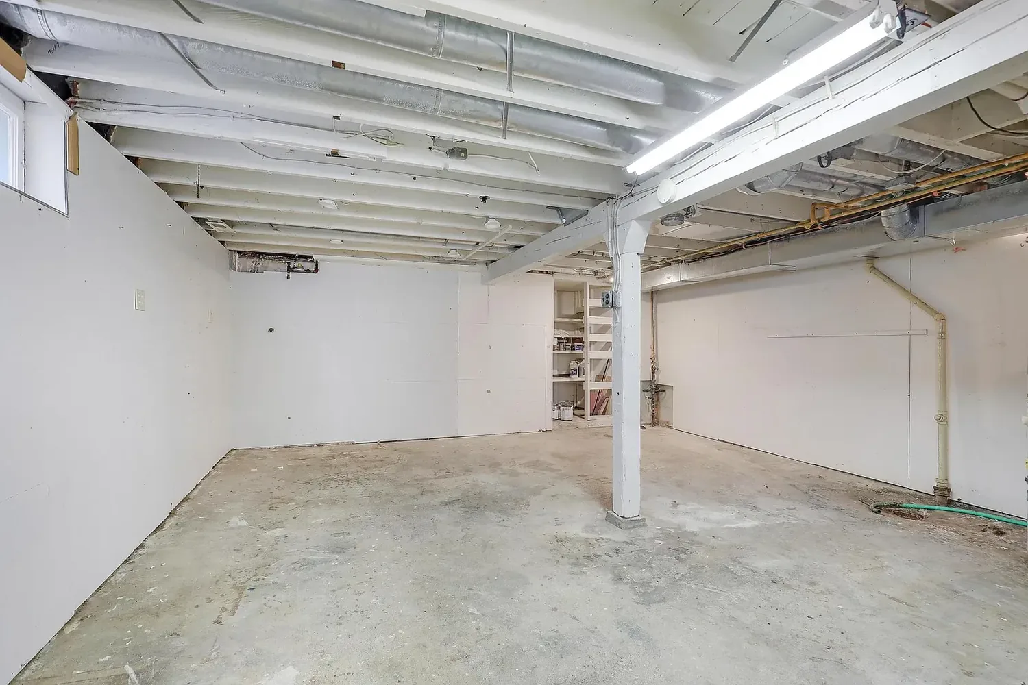 Basement after painting, with white walls and painted exposed ceiling joists